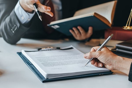 A person is signing a contract, likely with a lawyer. The image represents the legal industry, and provides visual context for web publishing of documents.